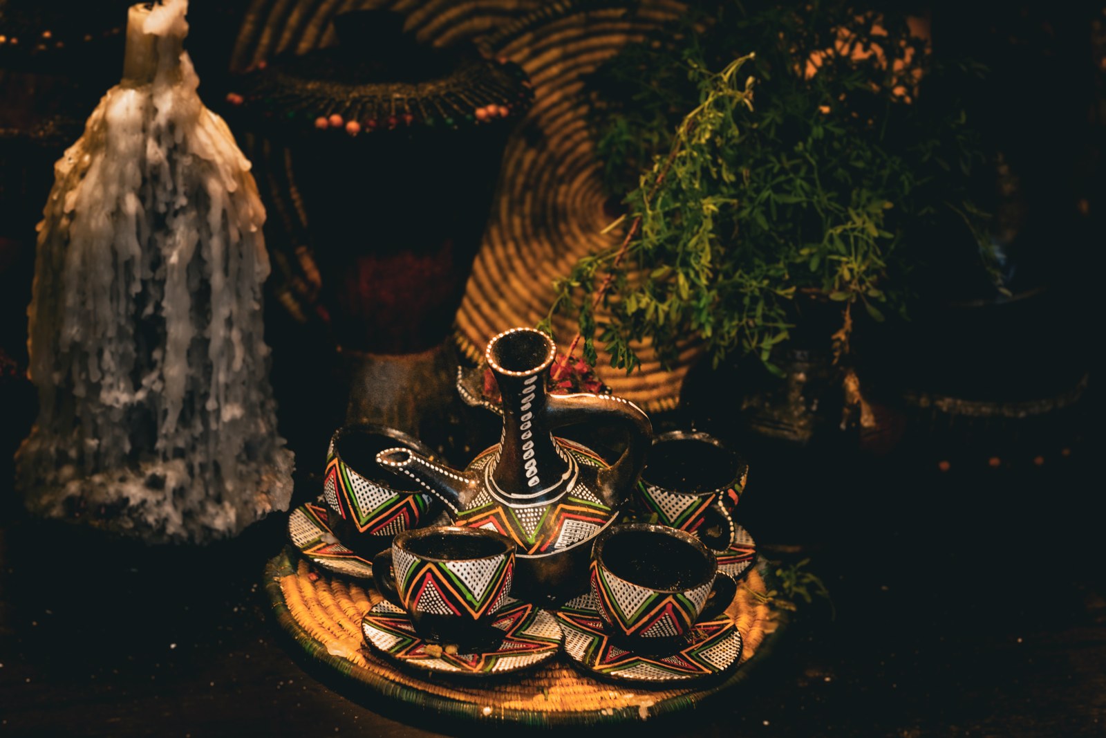 Painted clay jebena and small cups on a woven tray at a traditional coffee ceremony